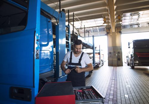 Truck mechanic servicing truck vehicle at workshop.